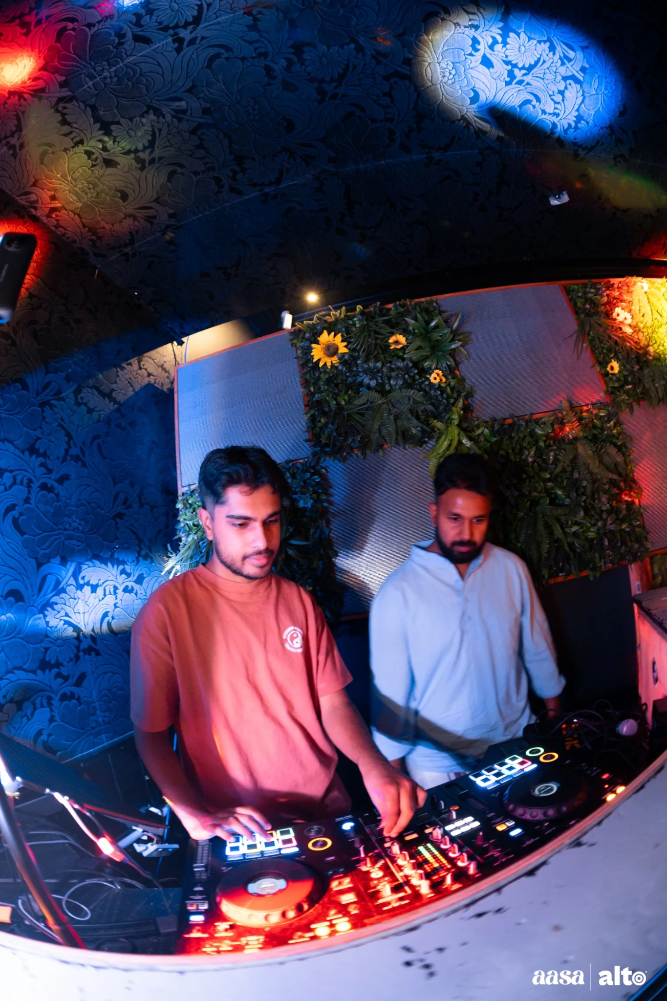 DJ Bhargav and another performer behind the decks under red and blue lights